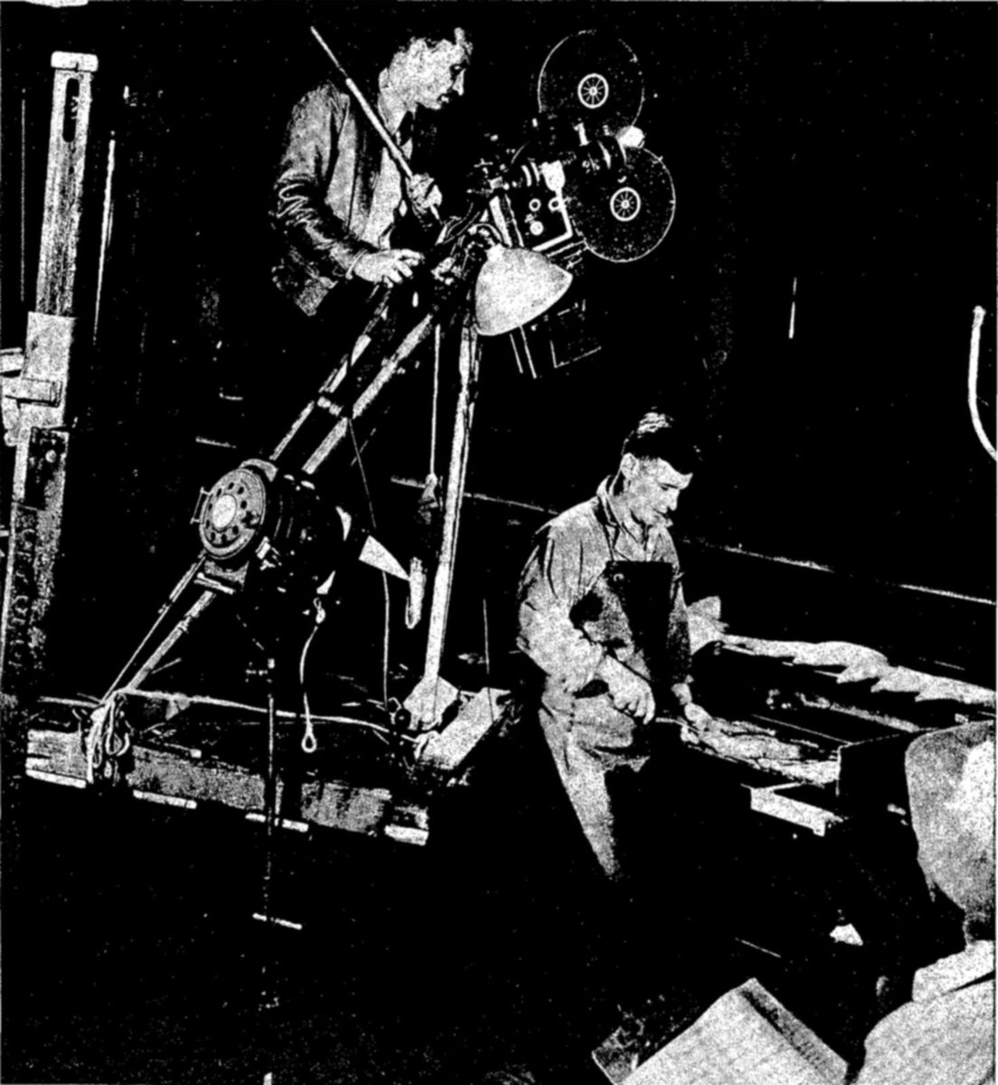 Motion pictures are used as educational aids in demonstrating approved methods of fish processing. Here the camera records fish filleting as part of a film which shows the handling of fish from its capture to the market. — A man stands behind a large motion-picture camera on a tall stand with a lamp, aimed down at an apron-clad worker who sits at a table cutting a fish.