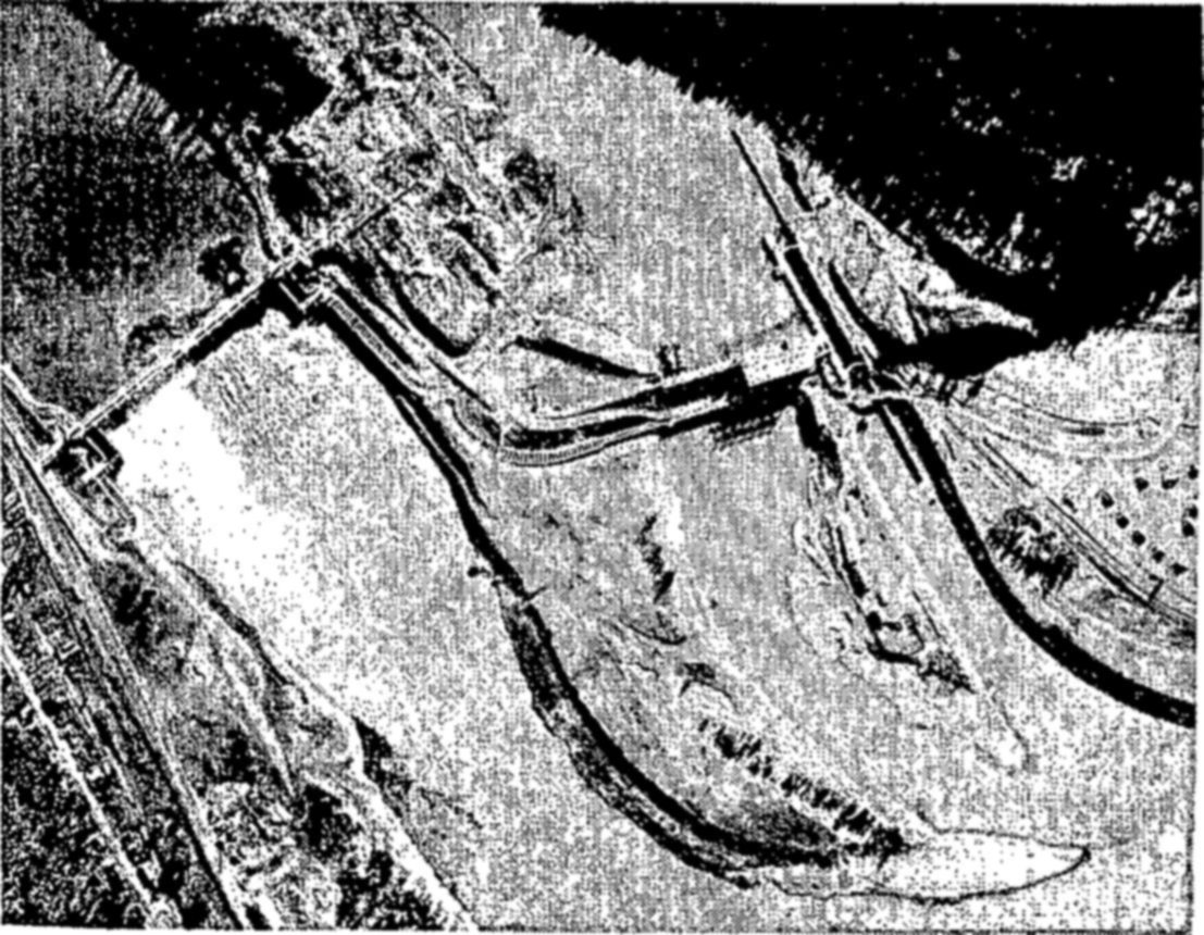 The largest fish ladders in the world are those at Bonneville Dam on the Columbia River. About 600,000 fish, mostly salmon, ascend these ladders each year. — An aerial view of a river crossed by a dam, with long curving channels running along the banks and across the stream below it.