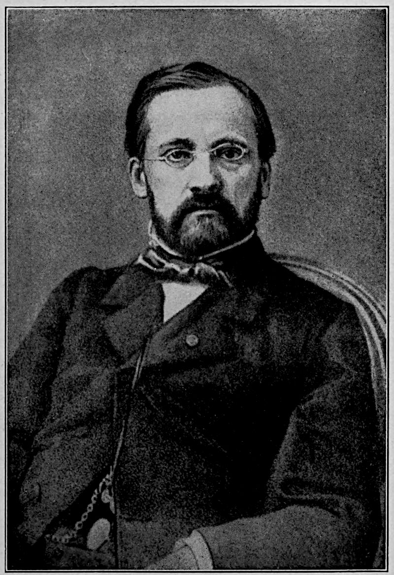 Pasteur at Forty-Five — A photograph of him seated in an armchair, with a full dark beard and small spectacles, a loose tie knotted at his collar, and a watch chain hanging against his dark coat.