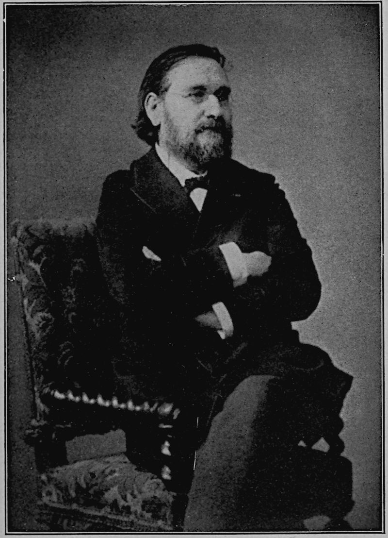 Élie Metchnikoff — A photograph of him seated sideways on a tapestry-covered chair, arms folded across his chest, with long hair swept back, a beard and spectacles, looking away to the right.