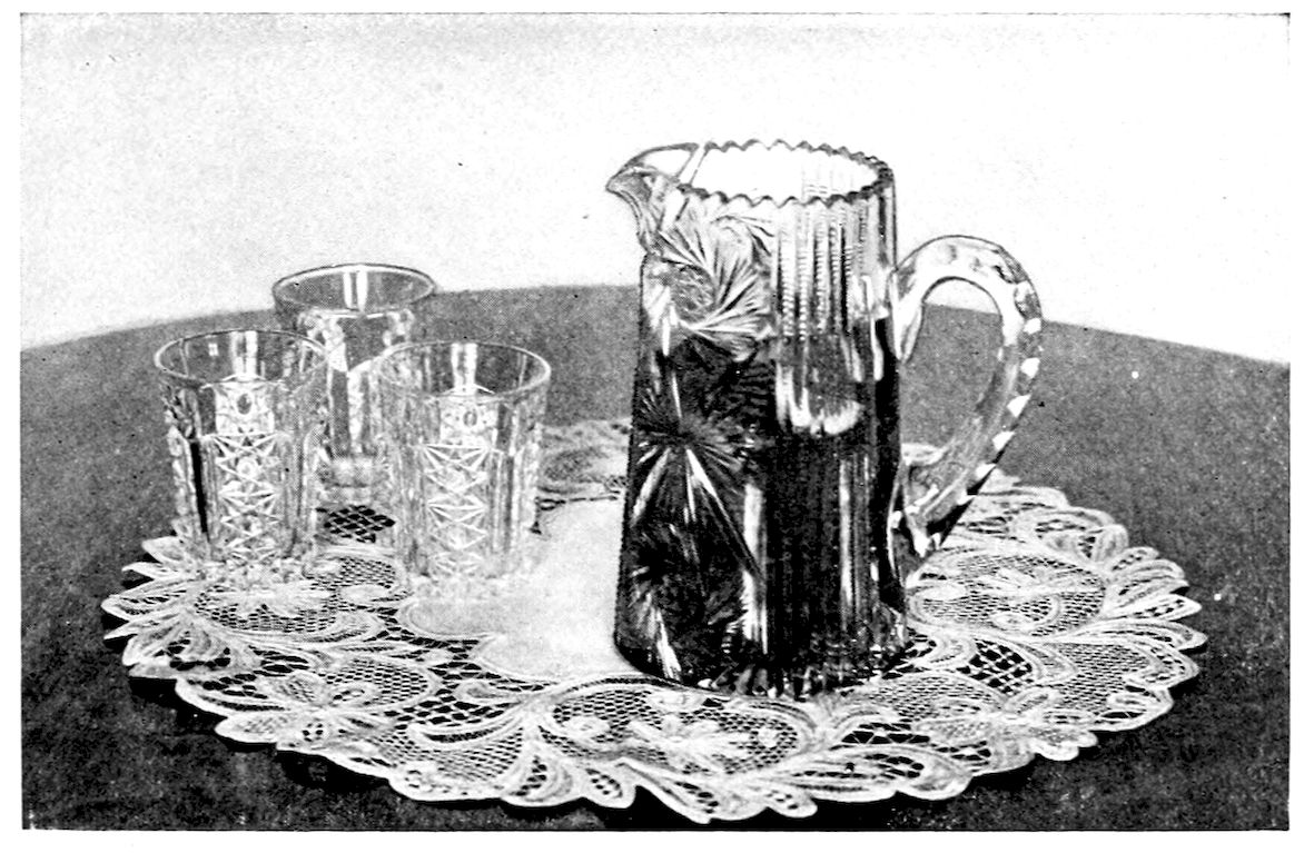 Claret Cup Service. — A tall cut-glass pitcher and three cut-glass tumblers on a round lace doily.