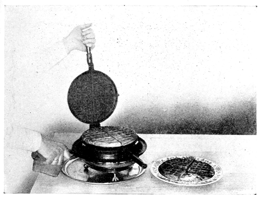 Waffles. — A hand lifts the upper half of a round waffle iron on its stand over the flame, showing a waffle marked in squares and cut in quarters; two quarters lie on a plate beside it.