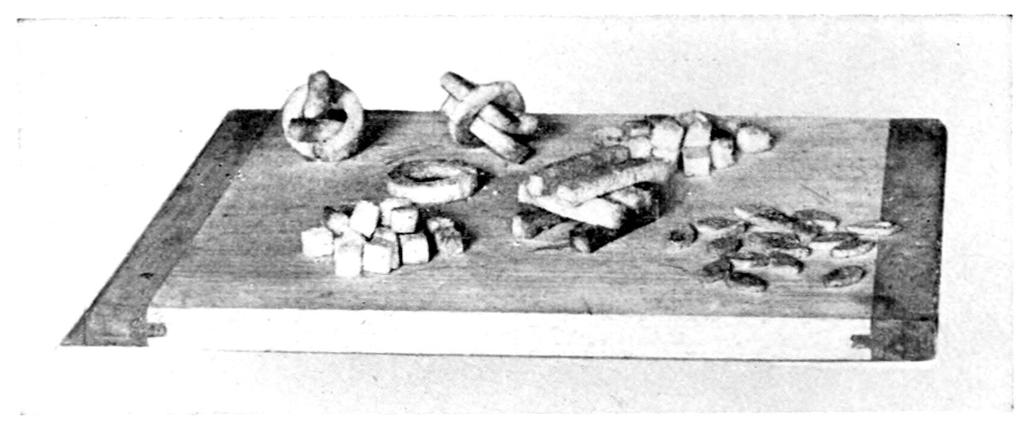 Croûtons; Imperial Sticks; Mock Almonds. — On a bread board: small cubes of croûtons, bread rings with three sticks laid through each, loose rings and sticks, and a scatter of small almond-shaped pieces.