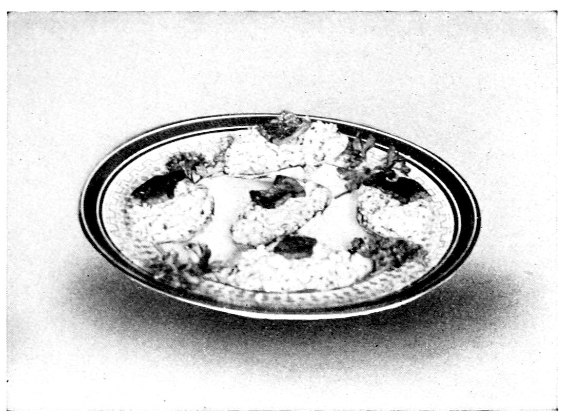 Clams Union League. — The refilled clam-shells lie close together on a round plate with a key-pattern border, each topped with a square of fried bacon, with sprigs of parsley between them.