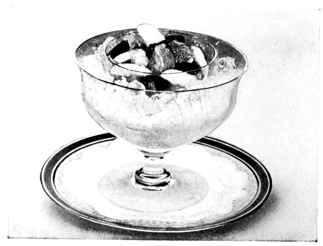 Fruit Cocktail. — The fruit is served in a double cocktail glass: a small inner glass heaped with pieces of banana, pineapple and strawberry sits in a larger stemmed glass packed with crushed ice, on a doily-lined plate.