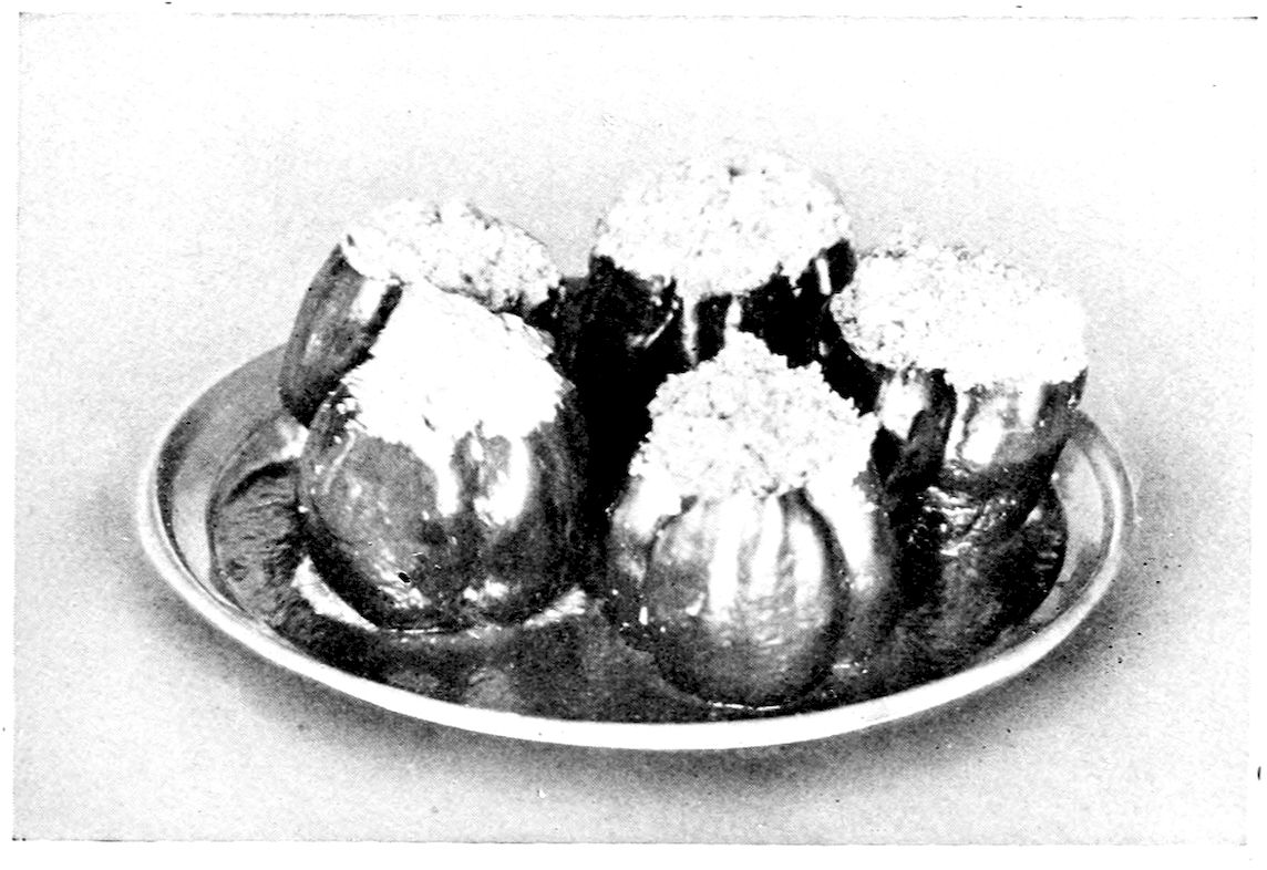 Stuffed Peppers. — Five stuffed peppers stand upright close together on a round platter, their tops cut off and the filling heaped above the rims under a browned crumb crust.