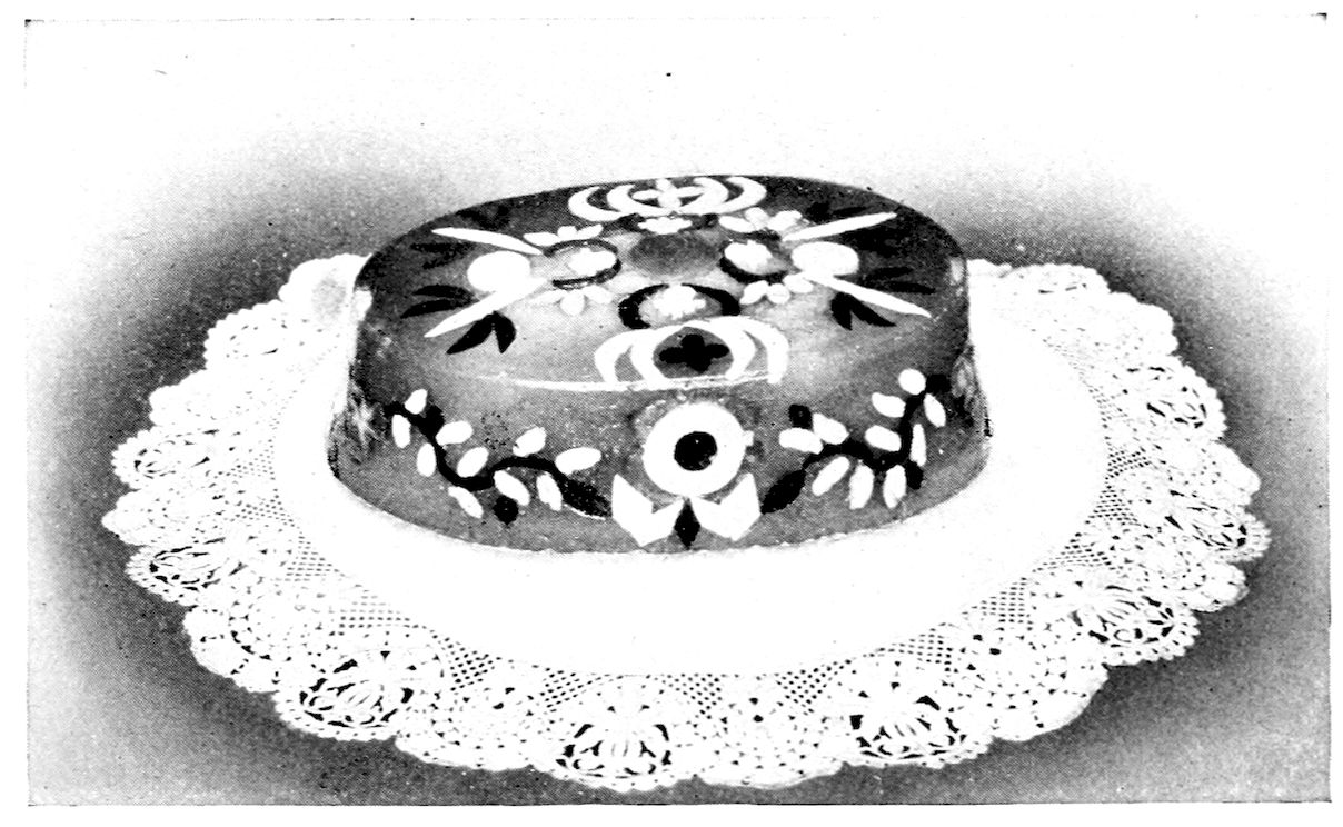 Capon in Aspic garnished with cooked yolks and whites of eggs cut in fancy shapes, pistachio nuts, and truffles. — A low oval mould of clear aspic turned out on a lace doily, the bird hidden within, with a pattern of flowers, scrolls and trailing vines set across its top and sides.