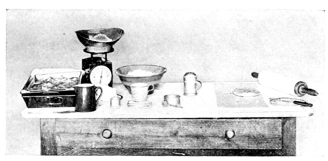Utensils and Materials for the making of Puff Paste. — A kitchen table set out with a dripping-pan of ice and butter, a pitcher, a spring scale weighing flour, a bowl, cups and a dredger, a pastry board and a rolling-pin with a knife.