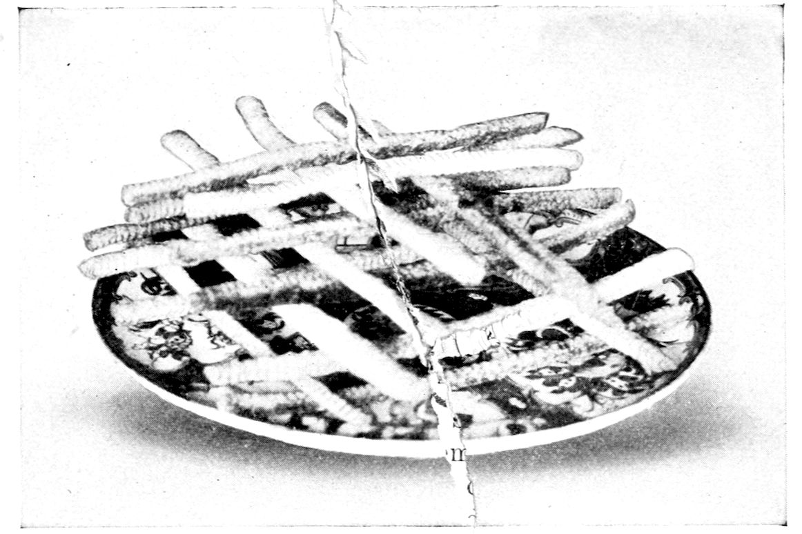 Cheese Straws. — Thin sticks of cheese straw piled crosswise in layers, log cabin fashion, on a patterned plate.