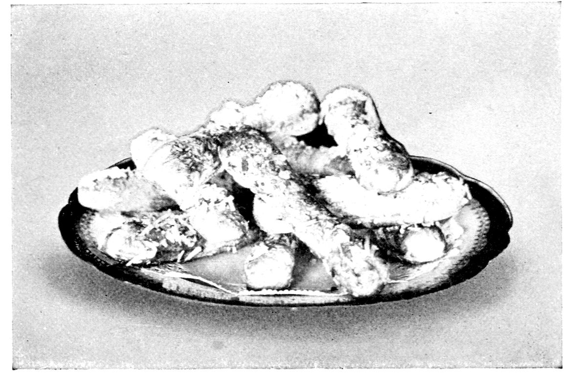 Cocoanut Tea Cakes. — Long lady-finger shapes of pastry, glazed and crusted with shredded cocoanut, piled loosely on a small oval dish.