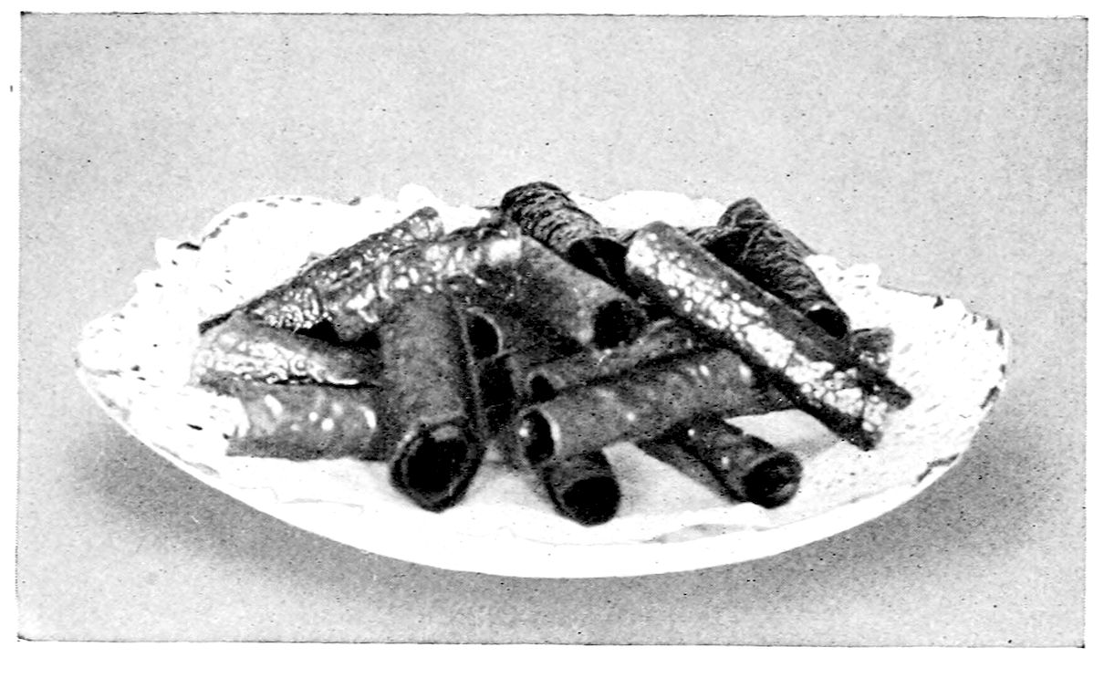 English Rolled Wafers I-II. — Thin lacy wafers rolled into hollow tubes are piled crosswise on a doily in an oval dish, their open ends showing.