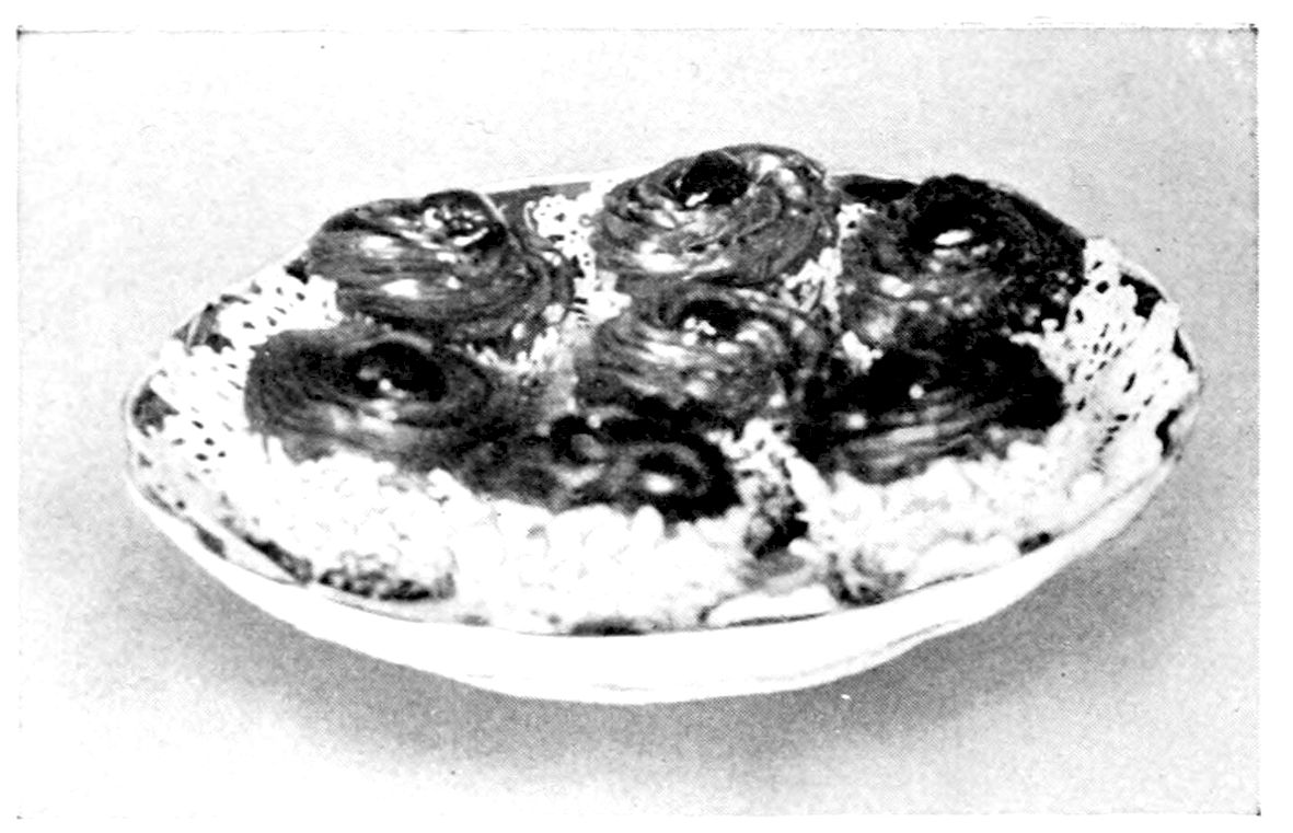 Mocha Cakes. — Small round cakes, their tops covered with coils of frosting forced from the rose tube and their sides rough with shredded cocoanut, stand close together on a lace doily in a shallow dish.