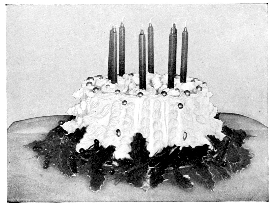 Ornamental Frosted Cake. — A tall ring cake covered in piped frosting, ruffled scrolls and silver balls, with eight tall slender candles standing in its top and a wreath of holly leaves and berries around its base.