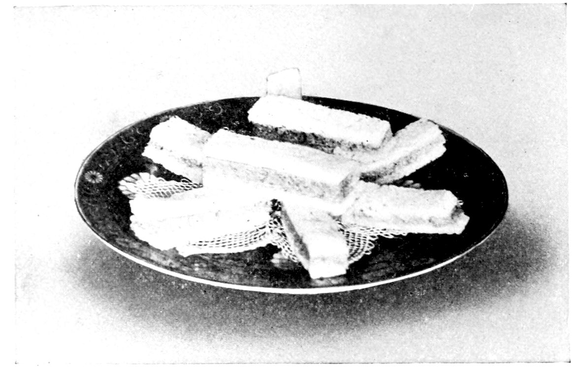 Bread and Butter Folds. — Oblong bread and butter folds with the crusts removed, some made in three layers with dark bread between white, are laid crosswise on a doily on a dark-bordered plate.