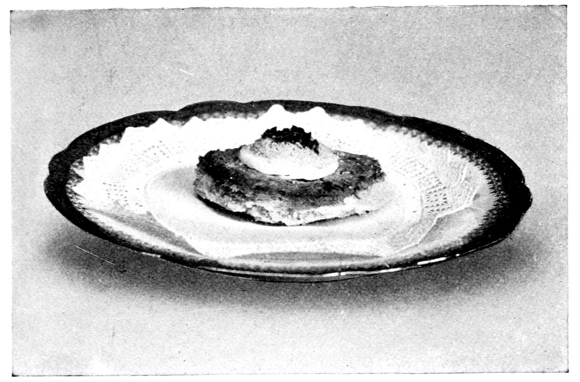 Lobster Canapé. — A single round of sautéd bread spread with lobster mixture and topped with a pale ring and a dark mound of garnish sits at the centre of a lace doily on a plate.