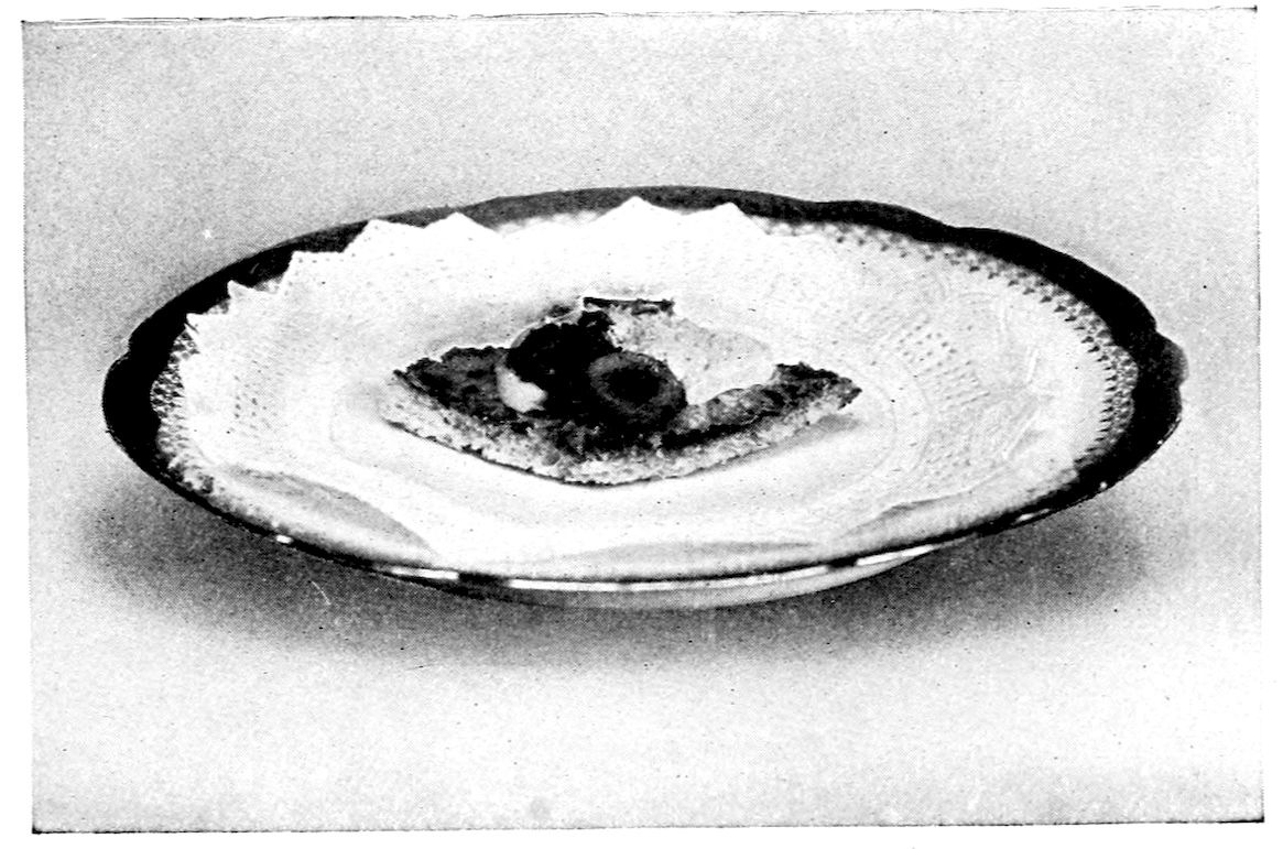 Canapé Martha. — A single fancy-shaped canapé topped with rings of hard-boiled egg white and a dark garnish sits in the middle of a lace doily on a plate.