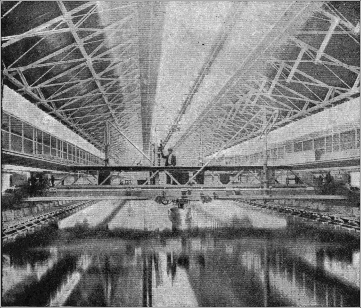 One of the experimental tanks — a long roofed-over bath with rails above the water carrying the towing carriage, from which the model ship hangs on a rod fitted with recording gear.