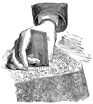 Fig. 49. — The right hand setting a card upright on a cloth-covered table, the fingers wrapped round it as it is pressed down; the little waxed prop is out of sight behind the card.