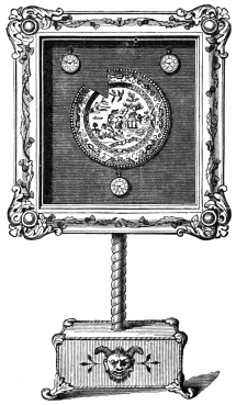 Fig. 295. — The picture frame on its pedestal base, with a willow-pattern plate in the centre and three watches round it; one piece of the plate’s rim appears to be missing.