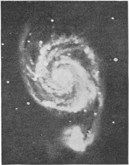 The Great Spiral Nebula. Photo: G. W. Ritchey — A spiral nebula seen face on, its bright centre wrapped in curling arms of luminous matter, with a smaller glowing mass hanging at the end of one arm below.