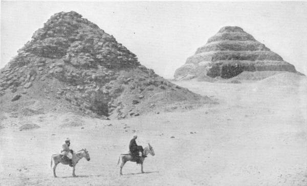 The Sakhara Pyramids. The Pyramid to the right, the step Pyramid, is the oldest stone building in the world. Photo: F. Boyer — Two pyramids rise from the desert: on the left a crumbling heap of loose stone, on the right the stepped pyramid in tiers; two men ride donkeys across the sand in front.