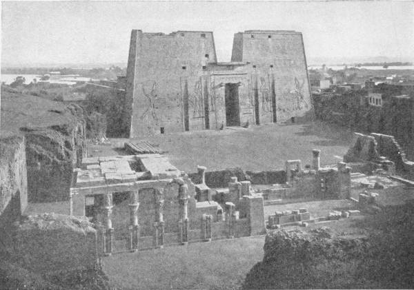 The Temple of Horus at Edfu — The two towering pylons of the temple, carved with huge figures either side of a central gateway, seen from above across a smaller ruined building of columns in the foreground.