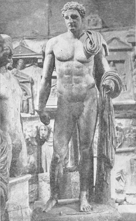Statue of Meleager. Note the progress in plastic power from the earlier wooden statue on left. Photo: Sebah & Foaillier — A marble statue of a young man standing naked with a cloak slung over his left shoulder and arm, set among other carvings in a crowded museum room; part of another figure shows at the left edge.