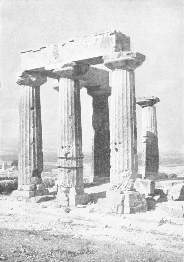 All That Remains of the Great Temple of Corinth. Photo: Fred Boissonnas — Five heavy fluted Doric columns still standing, three of them joined by a length of their stone lintel, on a bare hill above a wide plain.
