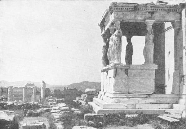 The Caryatides of the Erechtheum. The ancient sanctuary on the Acropolis at Athens. Photo: Fred Boissonnas — The porch of the Erechtheum, its roof carried by stone statues of robed women in place of columns, with the ruins of the Acropolis stretching away behind.