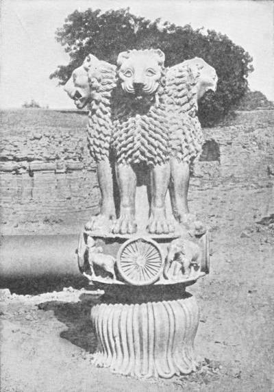 The Pillar of Lions. Capital of the Pillar (column lying on side) erected in Deer Park in the time of Asoka, where Buddha preached his first sermon. (From a print in the India Museum) — The carved capital of the pillar: lions seated back to back on a round drum carved with a wheel and animals, above a bell-shaped base of lotus petals, with the column itself lying on its side at the left.