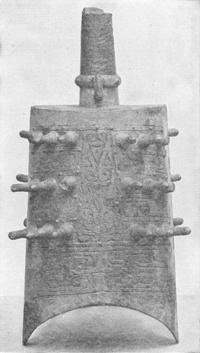Early Chinese Bronze Bell. Inscribed in archaic characters: “made for use by the elder of Hing village in Ting district;” latter half of the Chou Dynasty, Sixth Century B.C. (In the Victoria and Albert Museum) — A tall bronze bell with a flat-sided body flaring toward a curved lower rim, a cylindrical shank at the top, rows of projecting studs, and incised scroll patterns and characters.