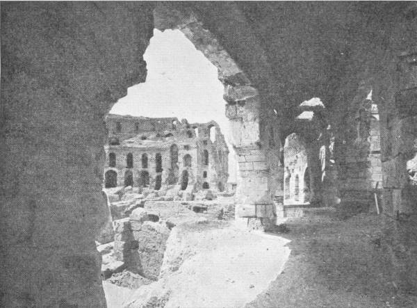 Relics of Roman Rule. Ruins of Coliseum in Tunis. Photo: Jacques Boyer — Looking through a broken stone arch in the dark lower passages of the amphitheatre, across rubble to its tiers of arches still standing on the far side.