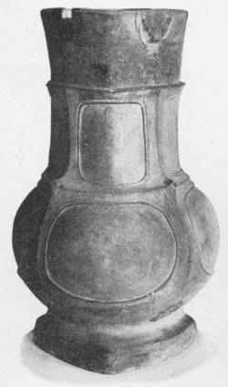 Vase of Bronze Form, Unglazed Stoneware. Han Dynasty ( B.C. 206–A.D. 220) (In the Victoria and Albert Museum) — A tall vase with a flared neck, a swelling body and a broad foot, its surface divided into plain rounded panels in imitation of a bronze vessel.