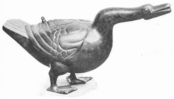 Chinese Vessel in Bronze, in Form of a Goose. Dating from before the time of Shi-Hwang-ti. Such a piece of work indicates a high level of comfort and humour. (In the Victoria and Albert Museum) — A bronze goose standing with its neck stretched out and its beak open, its wing feathers modelled in overlapping rows and a small knob on its back.