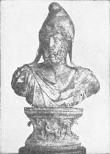 Bust of the Emperor Commodus, A.D. 180-192. Represented as the God Mithras, Roman, Circa A.D. 190. (In the British Museum) — A bust of a bearded man in a crested cap and a cloak, set on a carved pedestal.