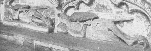 Crusader Tombs in Exeter Cathedral. Photo: Mansell — Stone effigies of two knights lie side by side under carved arches, each in mail with a shield on his arm, legs crossed and a sword across his body.