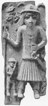 Another Ancient Negro Bronze of a European. (In the British Museum) — A bronze relief plaque of a tall bearded man in a helmet and pleated skirt holding a staff, with a much smaller figure standing beside him.