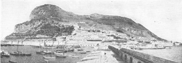 Gibraltar. Photo: C. Sinclair — The great Rock rises steeply behind the town and harbour, with sailing boats moored along the quay in the foreground.