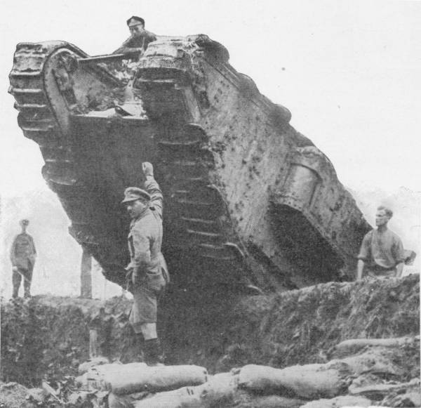 British Tank in the Battle of the Menin Road. The crew come out for a breath of fresh air during a lull. Photo: British Official — A tank rears up over the lip of a trench above a row of sandbags, a soldier sitting on its top and others standing about it.