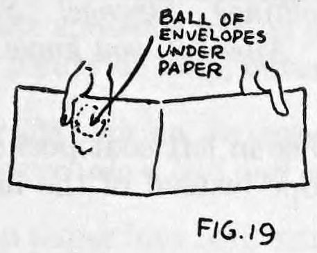 Fig. 19. — A sheet of newspaper folded over double, held by the right thumb in front, with a label pointing to the ball of envelopes hidden under the paper.