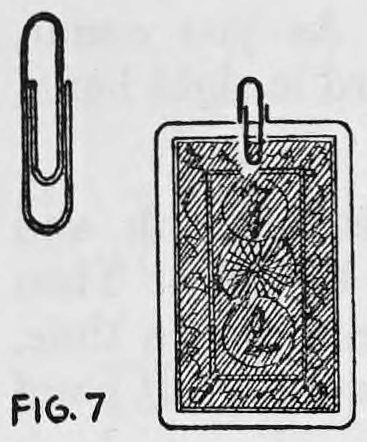 Fig. 7. — A wire paper clip shown alone beside a playing card, back out, with a second clip fastened over the top edge of the card.