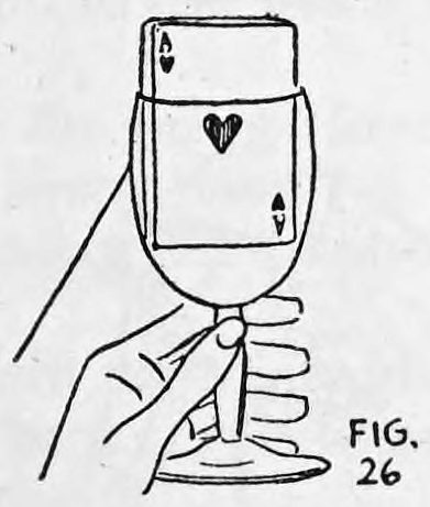Fig. 26. — A hand holds a glass tumbler by its stem, with the deck standing in the glass, faces toward the viewer, and the thread hanging down behind it to the left.
