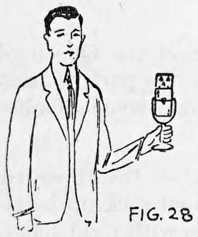 Fig. 28. — A man in a suit stands holding a glass with a deck of cards in his left hand, held out in front of him.