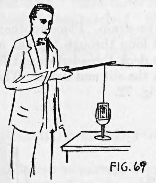 Fig. 69. — Thurston holds his wand out over a goblet of cards on a table; the thread from the deck runs up to the wand's eyelet, keeping it vertical above the deck.