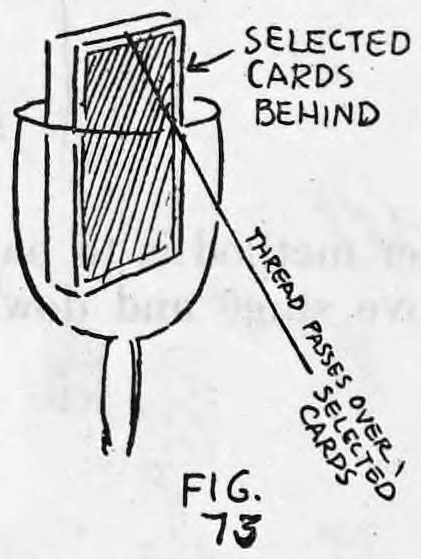 Fig. 73. — A goblet holding the deck with the three selected cards behind it, the thread passing over the selected cards and running off to the lower right.