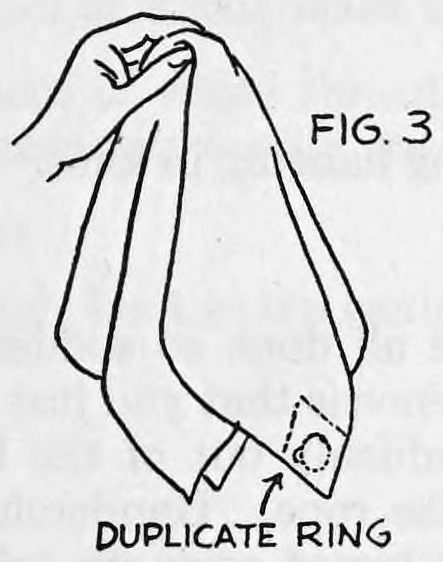 Fig. 3. — A hand holds the handkerchief by its center so it hangs down; the duplicate ring in its pocket shows at the lower rear corner, marked by an arrow.