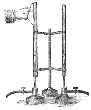 Three flames under their tubes, mounted side by side on one stand, each burner with its own tap. A note sounded at the right pitch will start the silent flame under the matching tube singing.