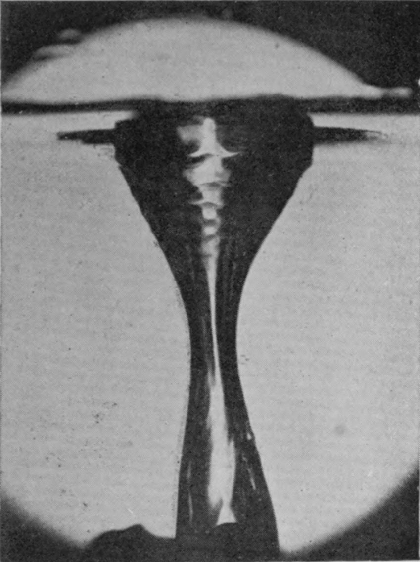6 0·045 sec. — The long hollow of air has narrowed to a waist near its lower end as it begins to divide, with the surface line crossing it near the top.