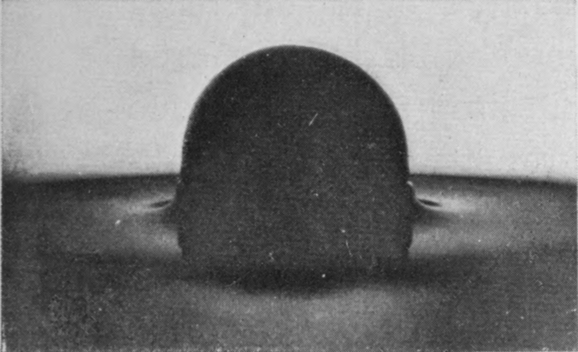 1 — The polished serpentine sphere is half into the pure glycerine, and the dark surface round it stays smooth, only slightly dimpled at the edges.