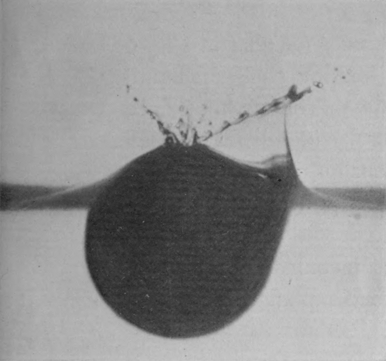 1 — The smooth film clings to the left side of the sphere; on the dusted right side the liquid has left the surface, opening a pocket of air and throwing out a line of droplets.
